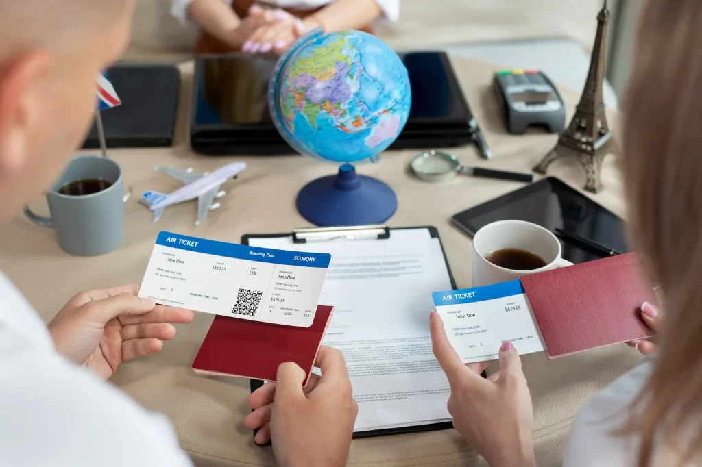 Manos revisando pasaporte y boletos frente a una laptop y un globo terráqueo.