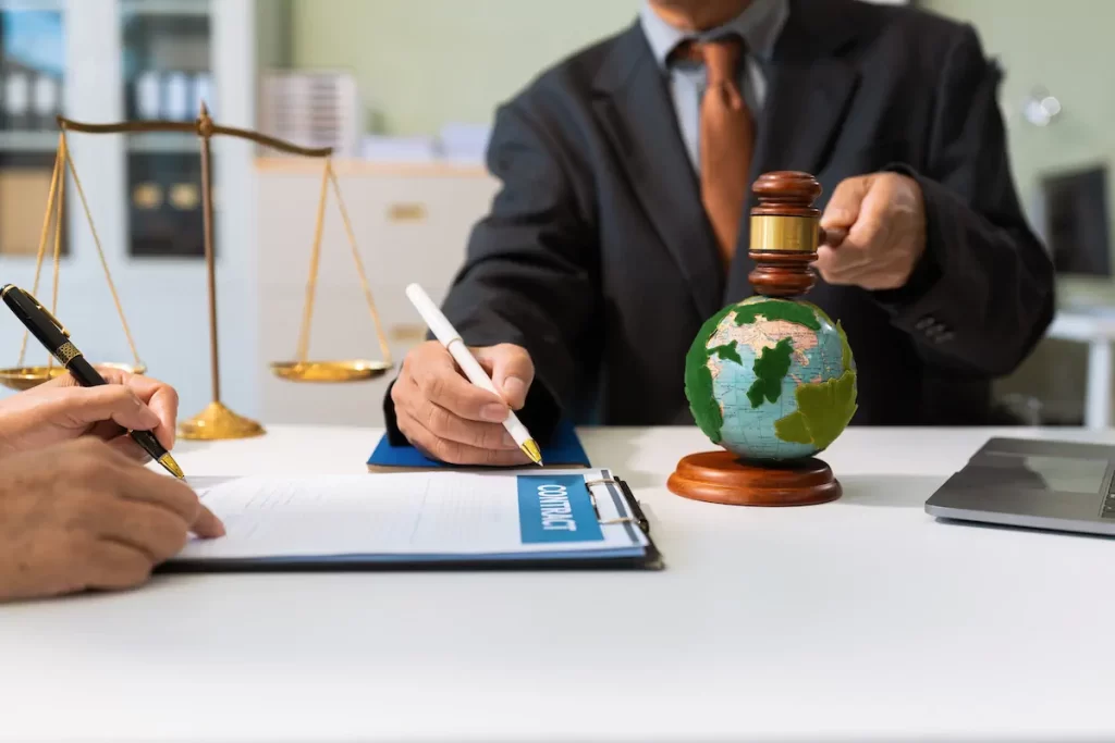 Persona firmando contrato junto a una balanza de la justicia y globo terráqueo.