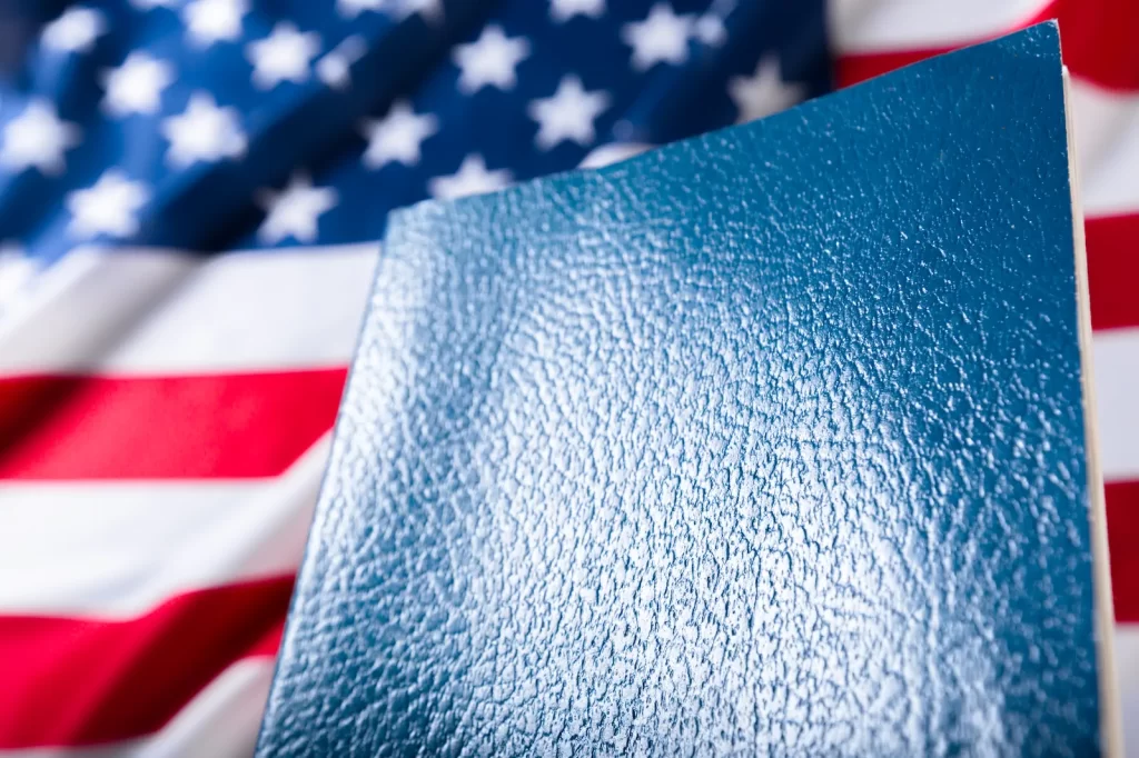Pasaporte azul frente a bandera de Estados Unidos en fondo desenfocado