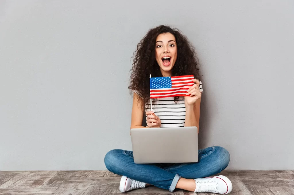 Mujer emocionada con una laptop y bandera de EE.UU. mientras prepara evidencias de lazos fuertes para su visa de turista.
