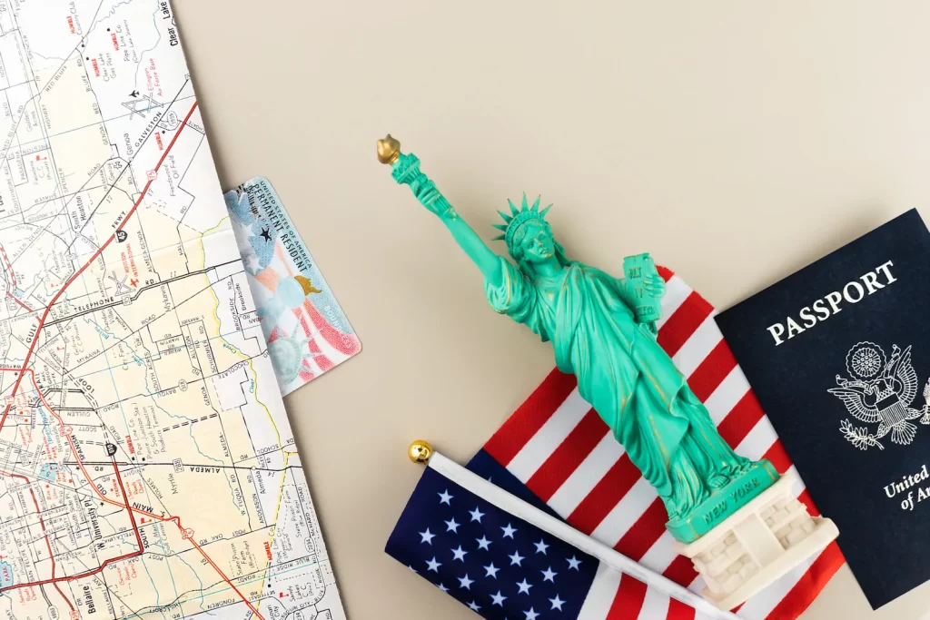 Mapa de viaje con una pequeña Estatua de la Libertad y bandera de EE.UU., representando planificación y vínculos previos al trámite de visa estadounidense.