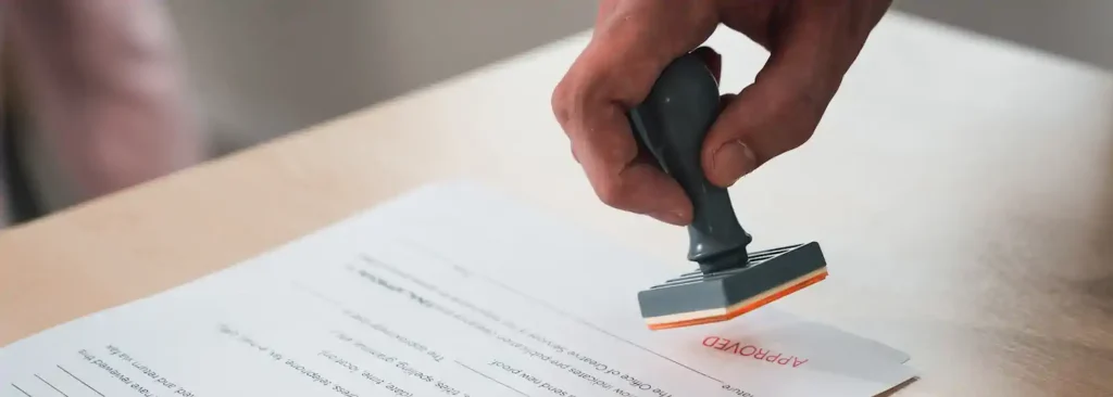 Mano colocando sello negro sobre documentos para trámite migratorio